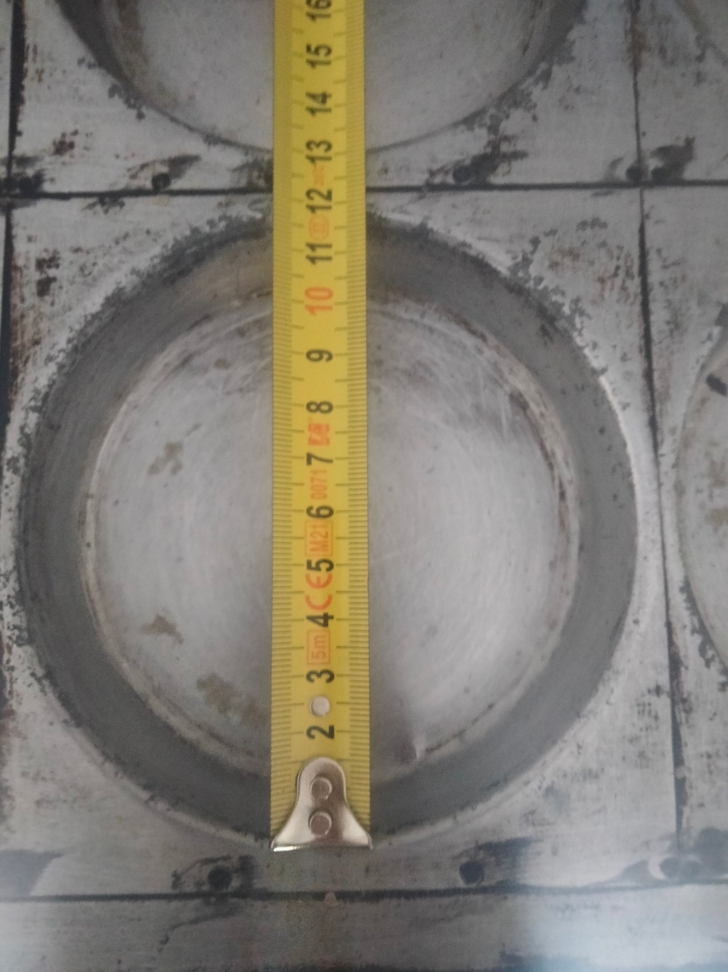 Teglia per focaccine 60x40x2 per un numero di 12 pizzette totali. Nell'immagine si vede uno stampo con un metro che misura la dimensino di 12 cm di diametro, teglia color grigio alluminio