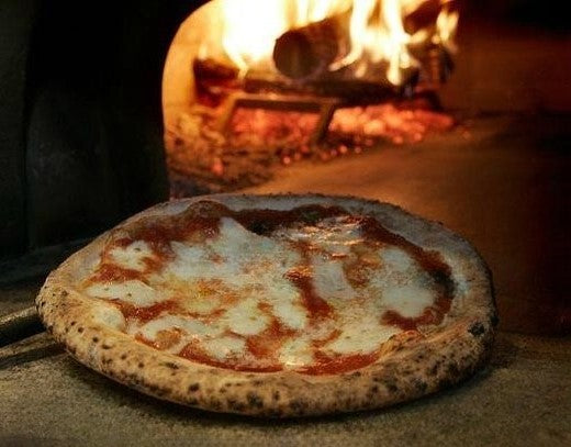 Pizza Margherita  Napoletana STG che esce da un forno  legna con fuoco sullo sfondo foto