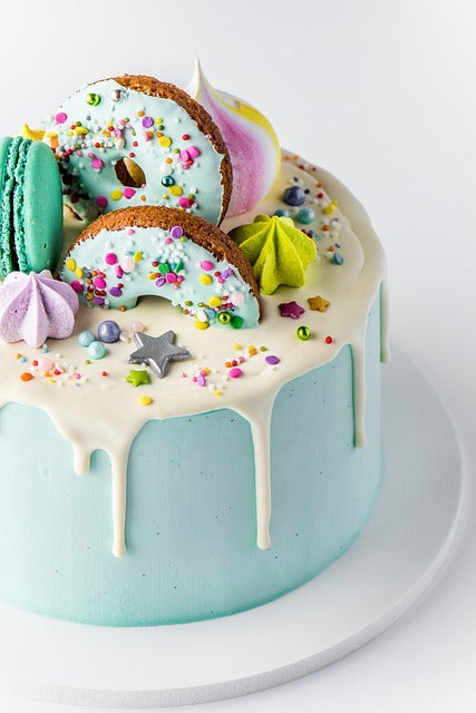 Torta di Compleanno Cake design, ricoperta di zucchero azzurro ai lati ed una colata di zucchero bianco sopra ed in centro meringhe e Donuts