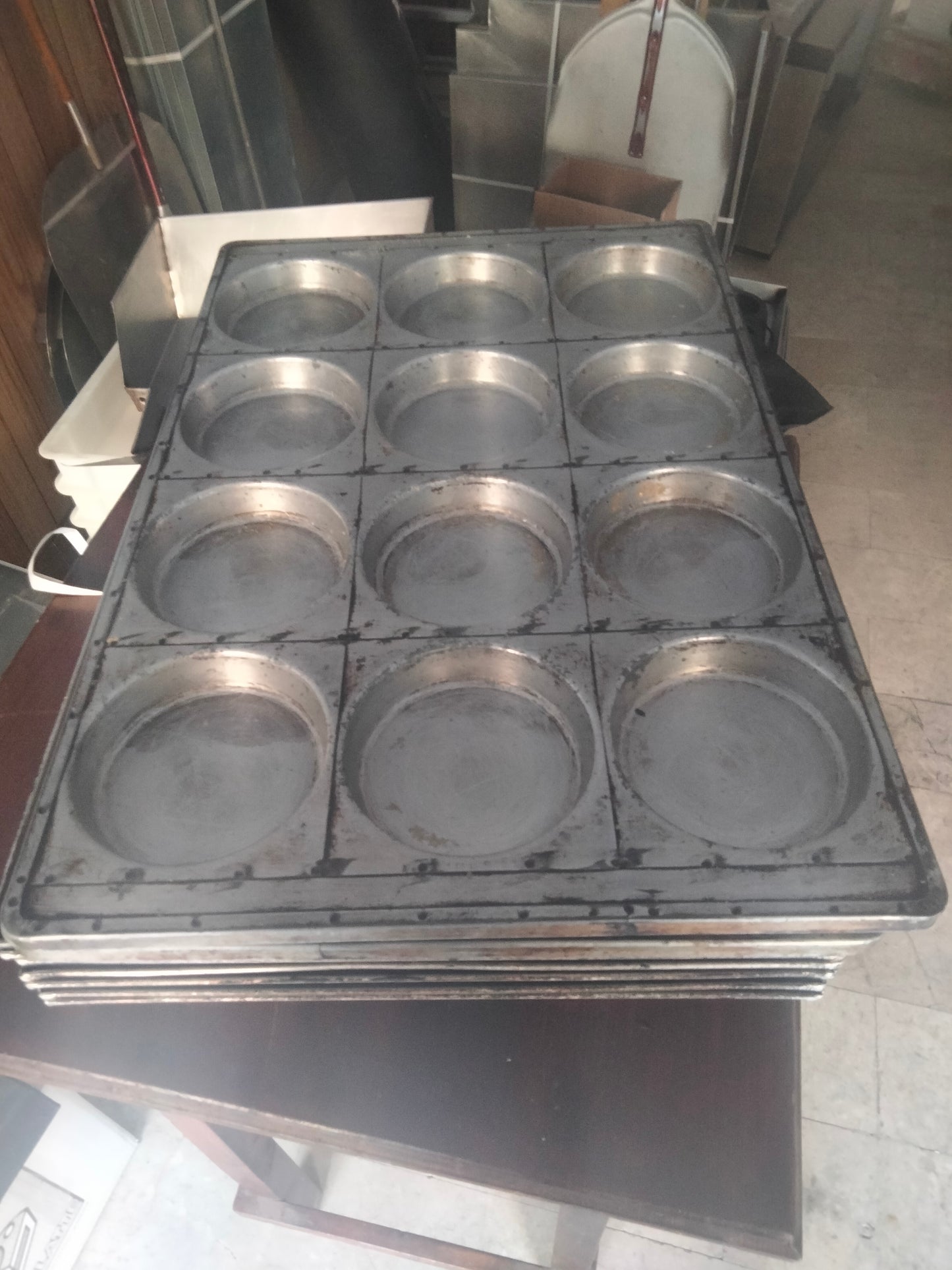 Teglia per focaccine 60x40x2 per un 12 pizzette rotonde. Nella foto si vede in primo piano una teglia per pizzette con 12 fori per poter produrre 12 pizzette, distribuiti su una linea 4x3, la teglie è grigia color alluminio