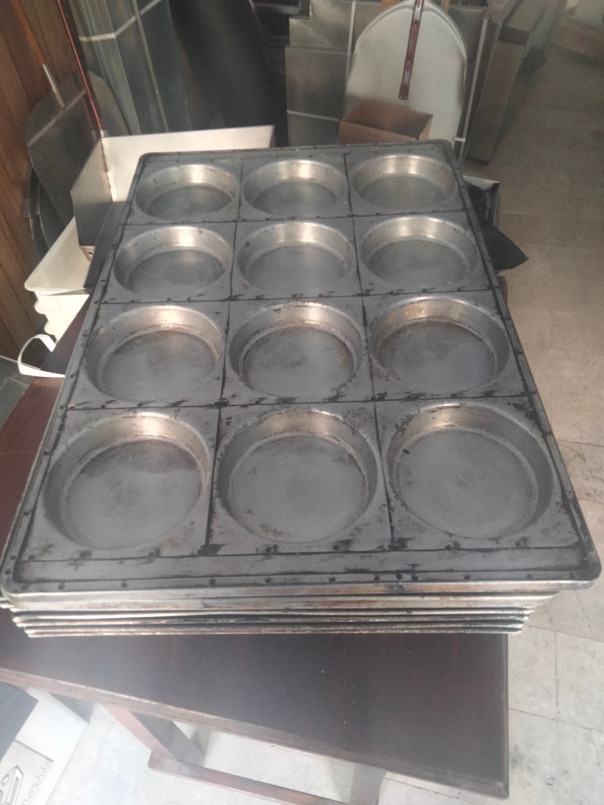 Teglia per focaccine 60x40x2 per un 12 pizzette rotonde. Nella foto si vede in primo piano una teglia per pizzette con 12 fori per poter produrre 12 pizzette, distribuiti su una linea 4x3, la teglie è grigia color alluminio